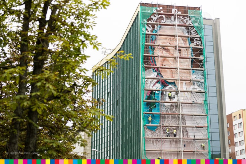 Mural w trakcie odmalowywania, ściana zasłonięta rusztowaniem